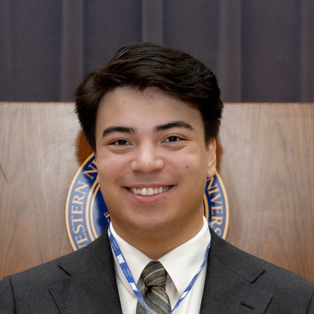 Portrait of Stephen Gibbons, smiling, in a charcoal suit jacket and striped tie